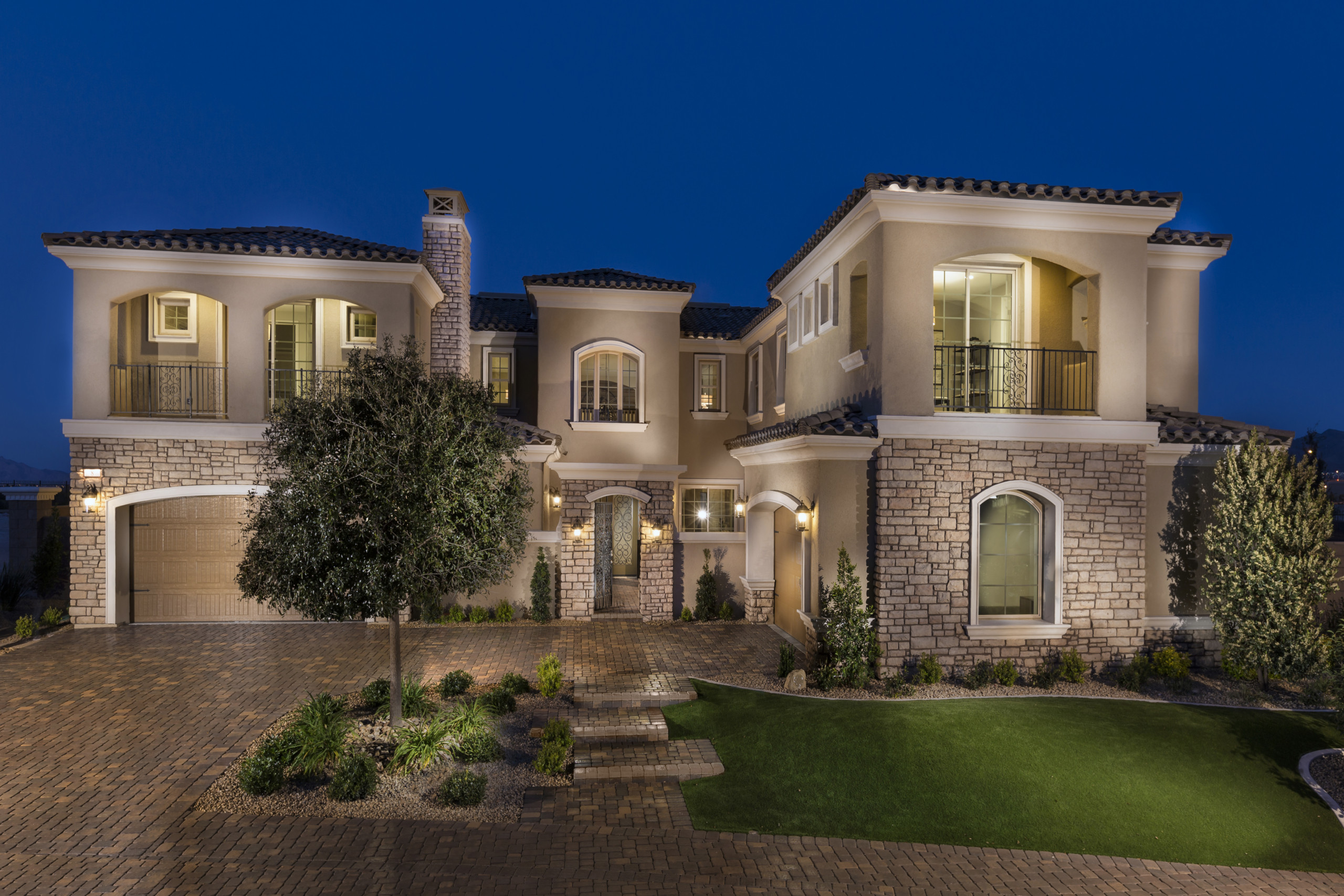Luxurious two-story home with illuminated exterior and landscaped yard at night.